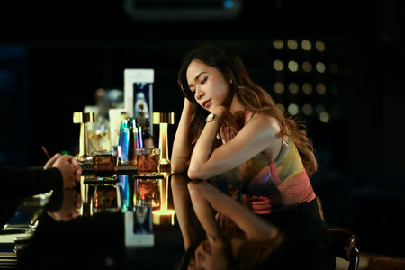 Young woman sitting at a dimly lit bar, lost in thought with a pensive expression and friend...