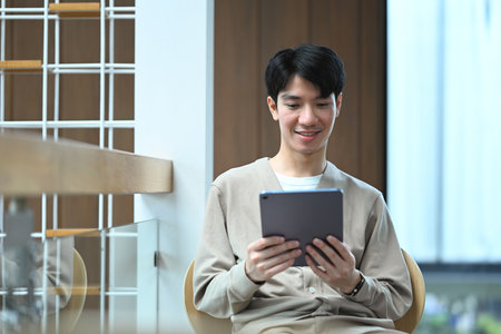 Portrait of smiling young asian man using digital tablet in modern cafe.の写真素材