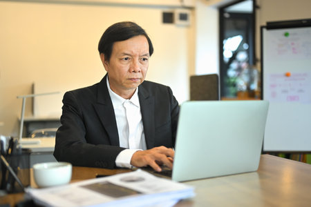 Focused asian senior businessman wearing black suit working in a modern office environment.の写真素材