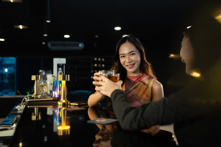 Attractive asian woman clinking glasses of whiskey with her friend at bar counter. Nightlife and friendship concept.の写真素材