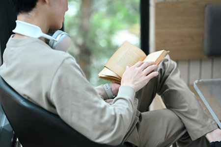 Smiling young asian man enjoying a peaceful moment, reading a book at a cafe.