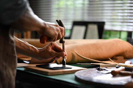 Asian male artisan carefully punching piece of leather at professional leather workshop.の写真素材