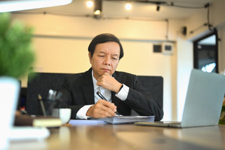 Middle aged businessman with a thoughtful expression working at desk in a modern office.の写真素材