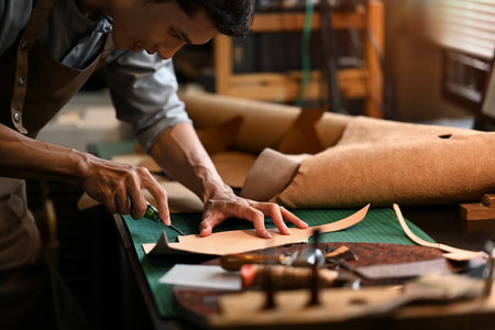 An artisan carefully using a sharp knife to shape the leather on cutting mat in his workshop.