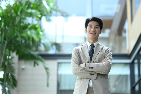 Portrait of smiling young businessman in a suit standing outdoors with arms crossed.の写真素材