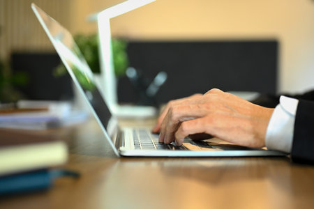 Close up shot of unrecognizable senior businessman hands typing on laptop keyboard.