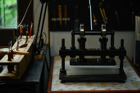 Manual press machine and various leather craft tools on wooden table in a local workshop.の写真素材
