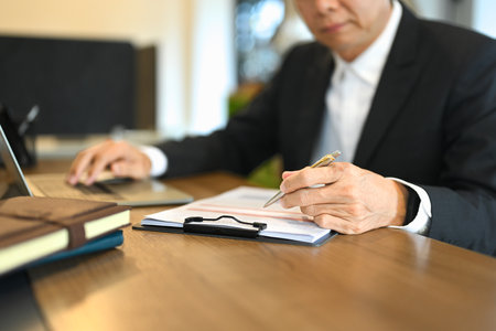 Cropped shot of mature businessman wearing black suit reviewing paperwork at his desk.の写真素材