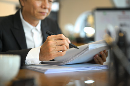 Experienced senior male investor in black suit reviewing statistics report at office desk.の写真素材