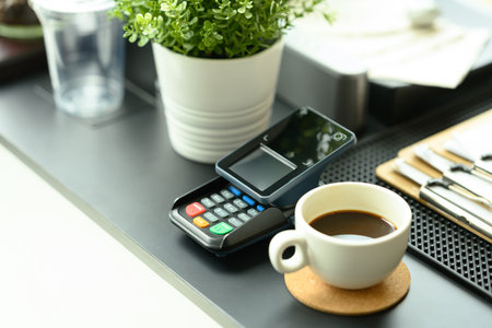 Payment terminal next to a coffee cup on counter of modern cafe ready for transactions. Contactless...