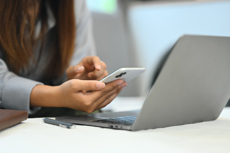 Young woman using mobile phone and working with laptop in living room.の写真素材
