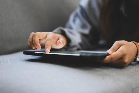 Close up image of unrecognizable woman hands using digital tablet, lying on couch at home.