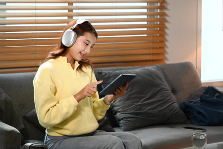 Charming young woman in wireless headphone surfing internet on digital tablet at home.の写真素材