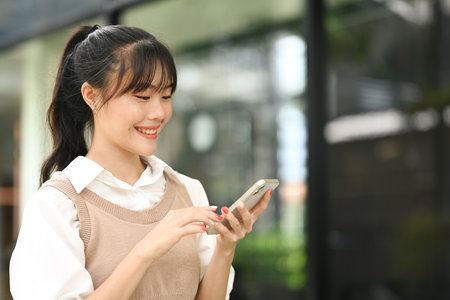 Beautiful young asian woman using smartphone outdoors. Lifestyle, technology and communication concept.の写真素材