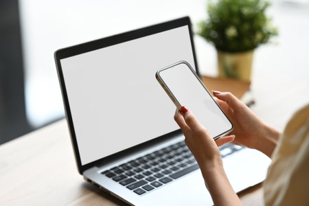 Close up image of young woman using smartphone in front of her laptop.の写真素材