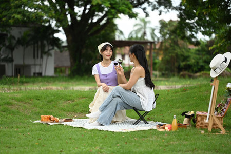 Two cheerful female friends toasting with red wine, enjoying a moment of relaxation in the park.の写真素材