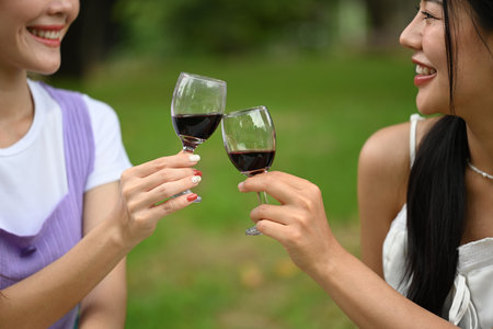 Cheerful beautiful women friends smiling warmly at each other while toasting with glasses of red wine.の写真素材