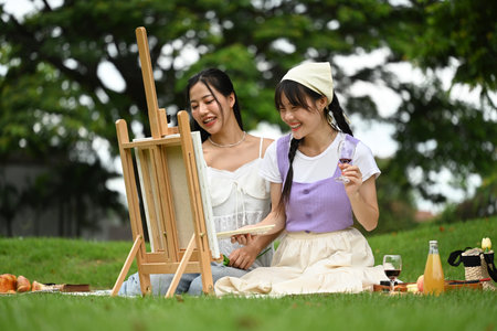 Two young asian women painting on easel with watercolors in a park.の写真素材
