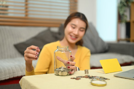 Cheerful young woman counting and stacking coins on a table. Saving money and financial...
