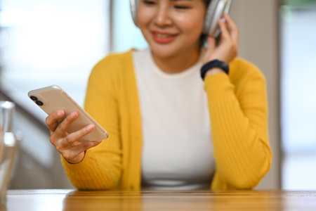 Close up of a young woman listening to music and using smartphone at kitchen counter top at home.の写真素材