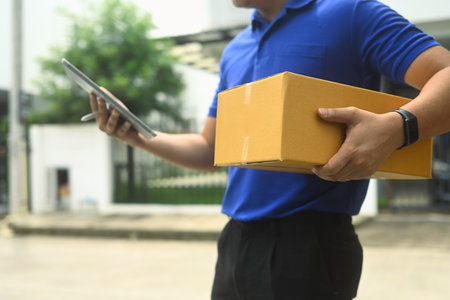 Delivery worker in blue shirt using digital tablet next to a vehicle filled with packages. Shipping and delivery services concept.の写真素材