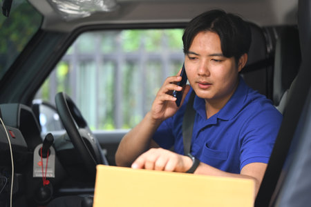 Young delivery man talking on mobile phone while sitting in a van. Shipping and delivery services concept.の写真素材