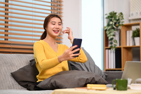 Happy young woman making video call on smartphone sitting on couch at home.の写真素材