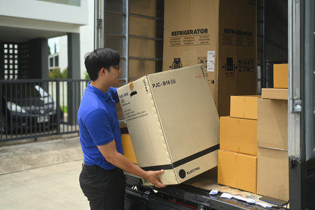 Delivery man wearing uniform unloading a large box from a truck. Shipping, logistics and...