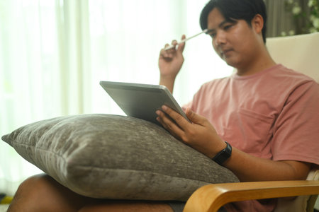 Concentrated male freelancer sitting on armchair and working with digital tablet at home.の写真素材
