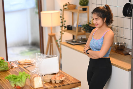 Smiling young woman preparing toast bread for breakfast at the kitchen table in the morning.の写真素材