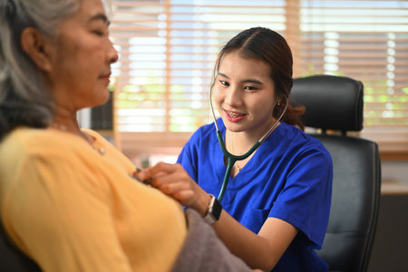 Female doctor in blue scrubs using a stethoscope examining elderly female patient.の写真素材