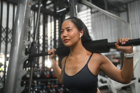 Focused sporty woman doing squat exercise with a barbell in a gym.