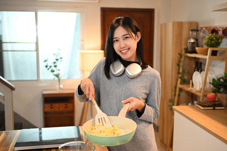 Pretty young asian woman preparing scrambled eggs for breakfast in the kitchen.