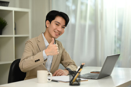 Professional businessman sitting at office desk and showing a thumbs up gesture.の写真素材