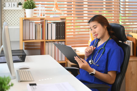 Smiling female doctor in a blue scrubs reviewing document in medical office.の写真素材