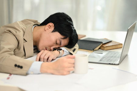 Tired young businessman sleeping at his office desk suffering stress or overworked.の写真素材