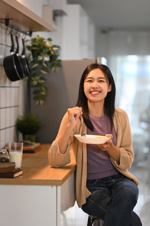 Pretty young asian woman eating a healthy breakfast at kitchen counter.の写真素材