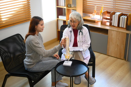 Senior female doctor pointing at vertebrae model while discussing spinal anatomy or treatment...