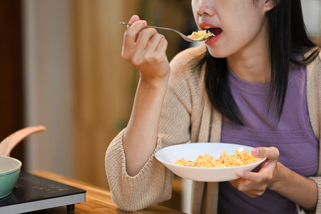 Cropped shot of young woman eating scrambled eggs for breakfast in kitchen.の写真素材