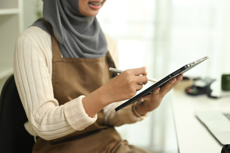 Smiling young muslim woman wearing hijab checking order on digital tablet. E-commerce and small business concept.の写真素材