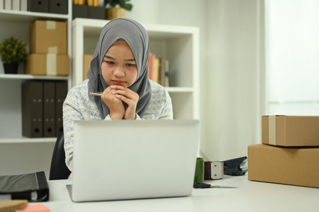 Asian Muslim woman small business owner using laptop for online marketing or checking purchase order.の写真素材