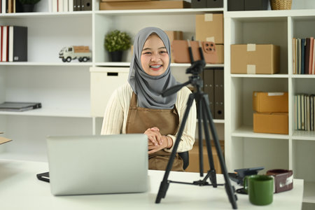 Smiling young Muslim woman conducting livestream from her home office. E-commerce, small business and online retail concept.の写真素材