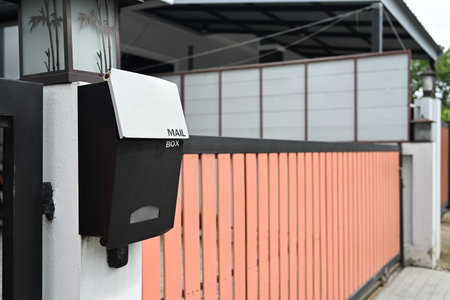 Modern mailbox mounted on a white pillar outside a house with a black and white color scheme.の写真素材