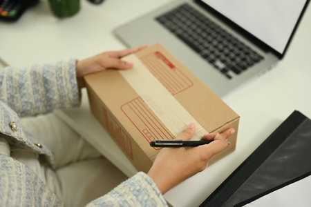 Close up female small business entrepreneur writing address on cardboard for delivery to customers.