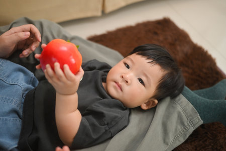Adorable little asian boy holding vegetable toys lying on sofa at home. Child care concept.