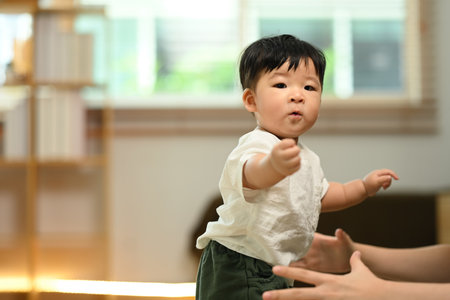 Delightful cute baby boy learning to walk with mother at home. Childhood and nurturing care concept.の写真素材