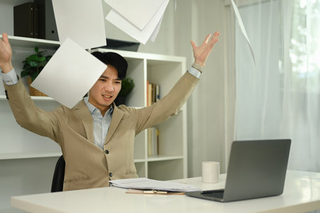Overworked angry businessman throwing papers in the air with emotional stress in his office.の写真素材