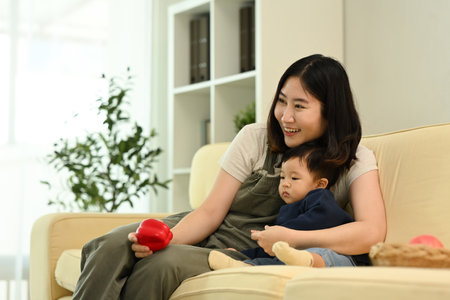 Joyful mother and her young child sitting on a cozy couch, enjoy spending time together at home.