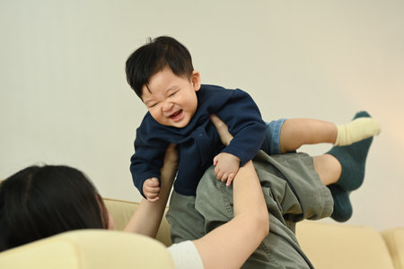 Playful young mother lifting her adorable little baby with her legs while lying on couch at home.