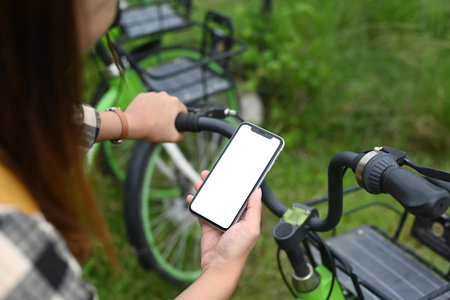Woman renting electric bicycle through smart phone. Concept of technology and eco friendly transport concept.の写真素材